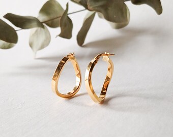 May include: A pair of gold-toned hoop earrings with a teardrop shape. The earrings are made of a smooth metal and have a polished finish.