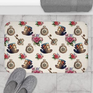 May include: A white bath mat with a repeating pattern of vintage pocket watches, keys, and top hats with gears. The background is a striped pattern of white and beige.