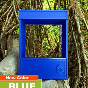 May include: A blue, rectangular, open-top display case with a small chameleon logo on the front. The case is sitting on a rock in a forest setting.