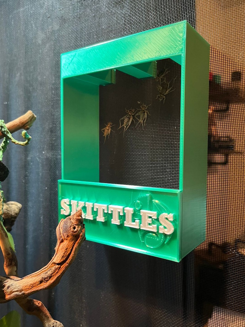 May include: A green 3D printed feeder with the word "SKITTLES" printed on the front. The feeder has three compartments and is designed to hold small insects.