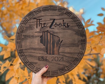 Könnte beinhalten: Ein rundes Schild aus dunkelbraunem Holz mit weißem Rand und einem gepunkteten Rand. Das Schild trägt den Text "The Zooks EST. 2021" und eine Silhouette des Bundesstaates Wisconsin.