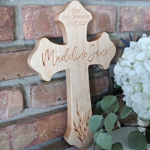 May include: A wooden cross with the words "First Holy Communion" and the date "05.07.2023" engraved on the top. The name "Madeline Jane" is engraved on the front of the cross.