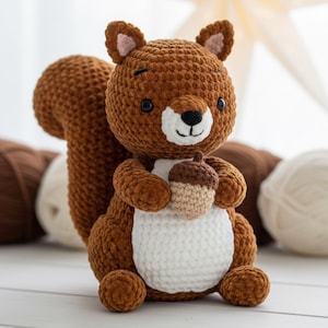 Peut inclure: Un jouet en forme d'écureuil en crochet marron fait à la main, avec une queue touffue, tenant un petit gland. L'écureuil a un ventre blanc, des yeux noirs et un visage souriant. Le jouet est en fil doux.