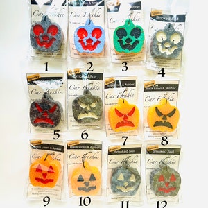 May include: Twelve individually packaged Halloween-themed car air fresheners in the shape of jack-o'-lanterns. Each package features a different scent and color combination, including black linen & amber, smoked suit, and amber. The packages are numbered 1 through 12.