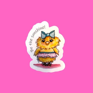 May include: A yellow chick with a blue bow and a pink polka dot skirt. The chick is standing on a pink background with the text "Be the sunshine!" written in black.