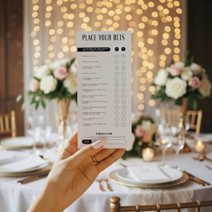May include: A white card with the text "PLACE YOUR BETS" is held up in front of a table setting. The card lists various betting options with check boxes. The background features a table set for a formal event with floral arrangements and soft lighting.