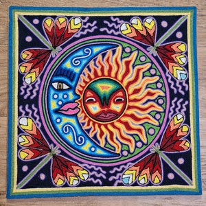 May include: A colorful embroidered artwork depicting a stylized sun and moon with a face. The sun is red, orange, and yellow with a green background. The moon is blue and pink with a purple background. The artwork is surrounded by a border of green, yellow, and blue.