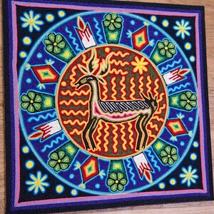 May include: Square, beaded artwork featuring a central deer figure with antlers, surrounded by a circular design. The artwork uses vibrant colors like blue, red, yellow, and green. The deer is outlined in black, with a pink and white body. The border is black, with a pink and purple trim.
