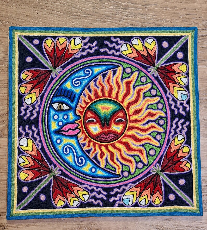 May include: A colorful embroidered artwork depicting a stylized sun and moon with a face. The sun is red, orange, and yellow with a green background. The moon is blue and pink with a purple background. The artwork is surrounded by a border of green, yellow, and blue.