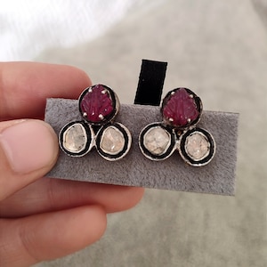 May include: A pair of silver earrings with three round, clear gemstones and a red, carved gemstone in the center of each earring.