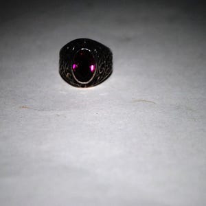 Op de afbeelding: Een zilveren ring met een donkerpaarse ovale edelsteen.