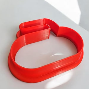 May include: A bright red plastic cookie cutter shaped like a curling stone. The cutter has a handle and a raised rim.