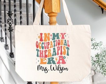 May include: A natural canvas tote bag with the text "In My Occupational Therapist Era" in colorful retro font. The text "Mrs. Wilson" is printed below the main text.