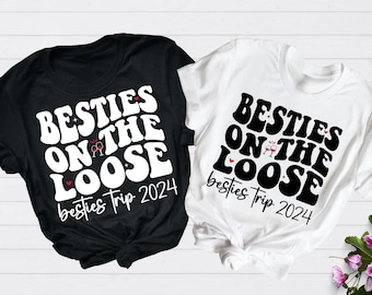 May include: Two t-shirts with the text "Besties on the Loose" and "Besties Trip 2024" in a retro font. One shirt is black and the other is white.