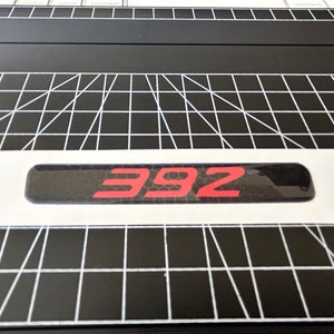 May include: A black and red car emblem with the number 392 in red.