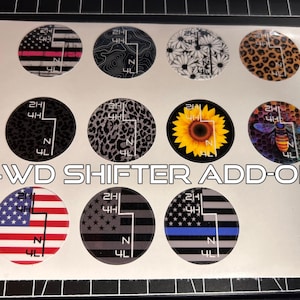May include: A sheet of 4WD shifter add-on decals with various designs. The designs include American flags, leopard print, a sunflower, and a bee. The text "4WD SHIFTER ADD-ON" is printed in white.