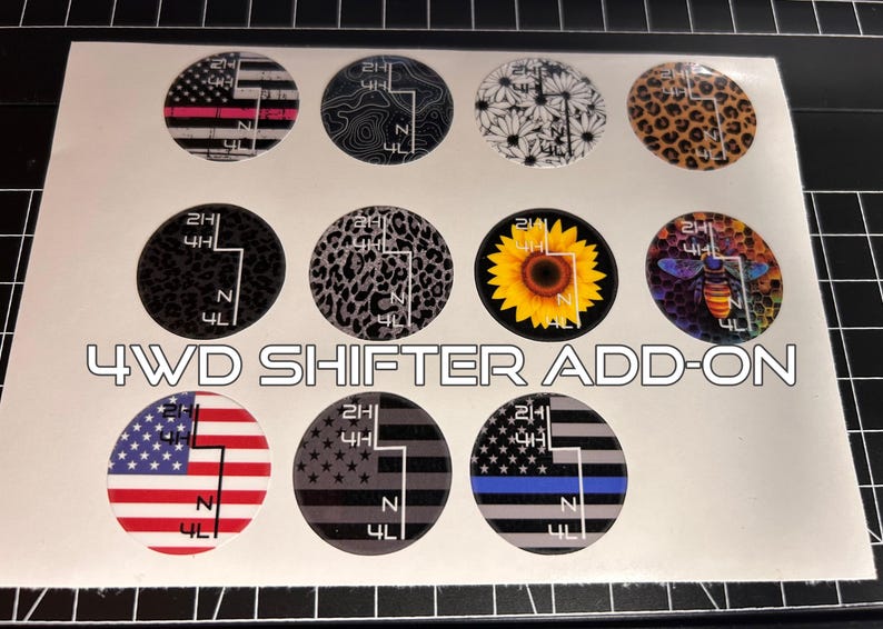 May include: A sheet of 4WD shifter add-on decals with various designs. The designs include American flags, leopard print, a sunflower, and a bee. The text "4WD SHIFTER ADD-ON" is printed in white.