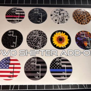 May include: A sheet of 4WD shifter add-on decals. Designs include American flag, leopard print, floral, and a sunflower. The text "4WD SHIFTER ADD-ON" is printed in white. Each decal has a gear shift pattern.