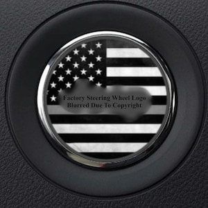 May include: A black and white American flag steering wheel cover with a silver trim. The text "Factory Steering Wheel Logo Blurred Due To Copyright" is printed on the cover.