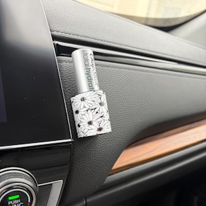 May include: A ChapStick total hydration lip balm with a white and black daisy floral pattern. The silver cap has the words "ChapStick total hydration" printed on it. The lip balm is resting on a black surface.