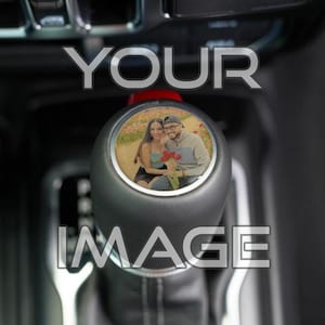 May include: Black gear shift knob with a personalized photo insert. The photo shows a couple holding flowers. The text "YOUR IMAGE" is overlaid on the image in a silver font. The knob is set against a dark interior.