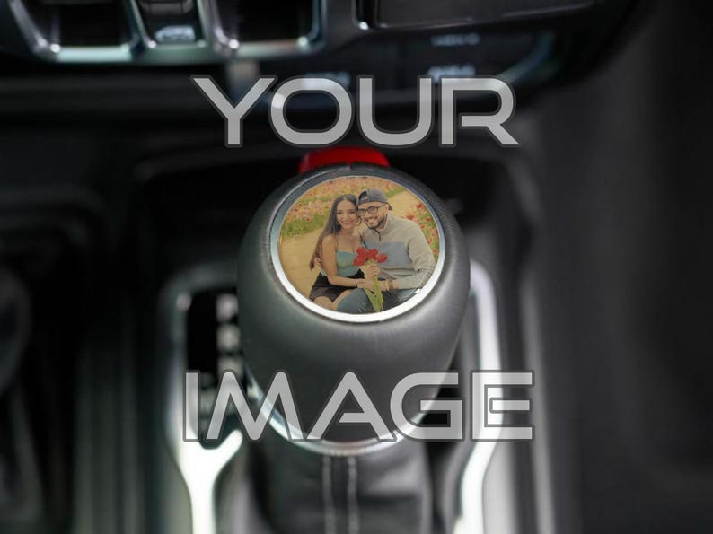 May include: Black gear shift knob with a personalized photo insert. The photo shows a couple holding flowers. The text "YOUR IMAGE" is overlaid on the image in a silver font. The knob is set against a dark interior.