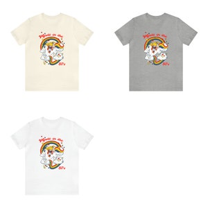 May include: Three t-shirts with a retro cartoon unicorn design. The shirts are in cream, grey, and white.