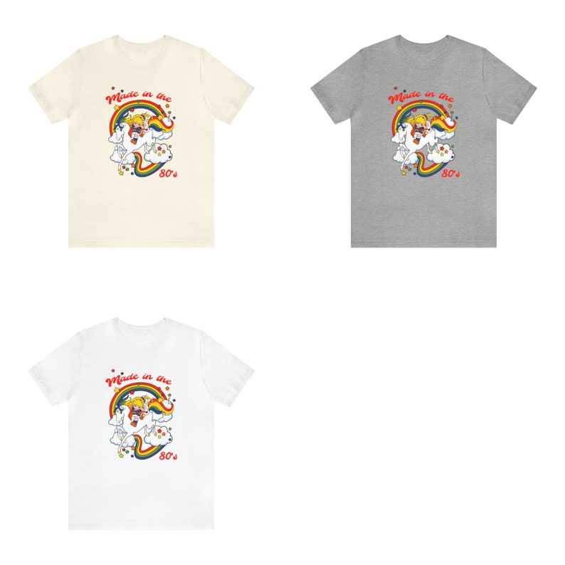 May include: Three t-shirts with a retro cartoon unicorn design. The shirts are in cream, grey, and white.