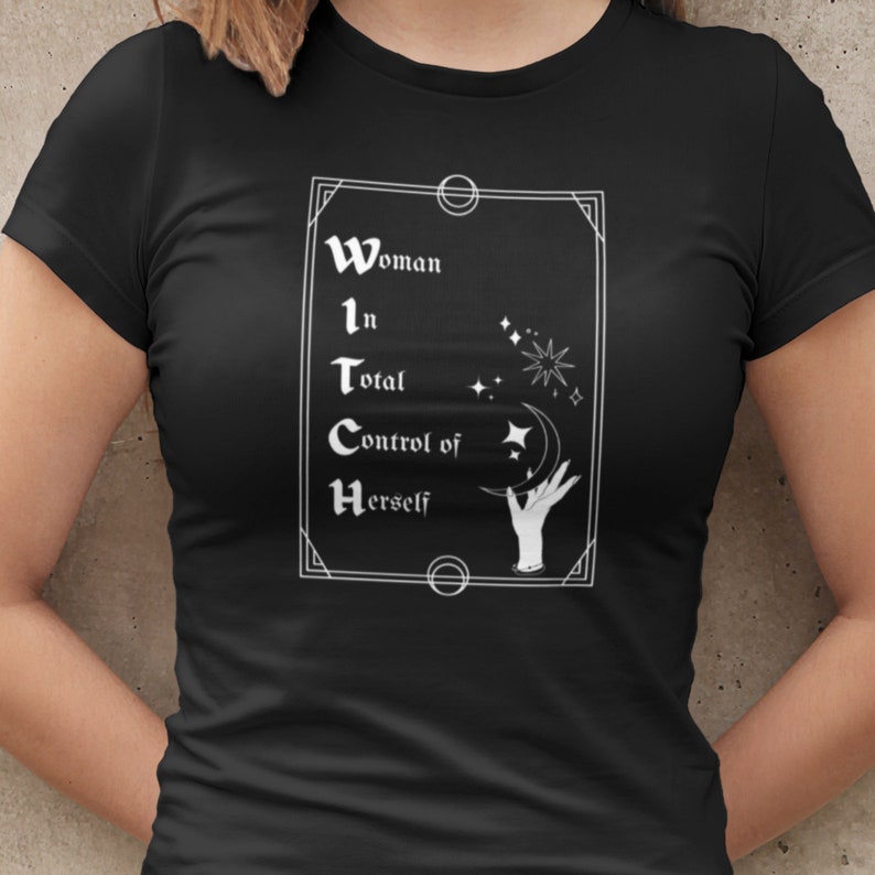 Pode incluir: Camiseta preta com um gr&aacute;fico branco. O gr&aacute;fico diz "Woman in Total Control of Herself" dentro de uma moldura retangular. O design inclui estrelas, uma lua crescente e uma m&atilde;o.