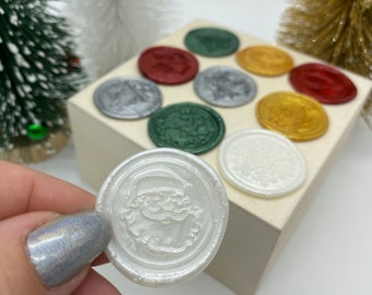 May include: A set of ten wax seals in various colors and designs, including a white seal with a Santa Claus design. The seals are arranged on a white surface.