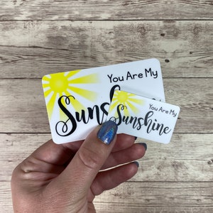 May include: Two white cards with black text and a yellow sun graphic. The larger card says "You Are My Sunshine" and the smaller card says "You Are My Sunshine".