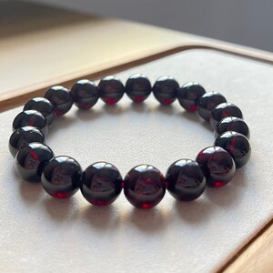 May include: A bracelet made of dark red gemstone beads. The beads are round and smooth, and they are strung together on a clear elastic cord.