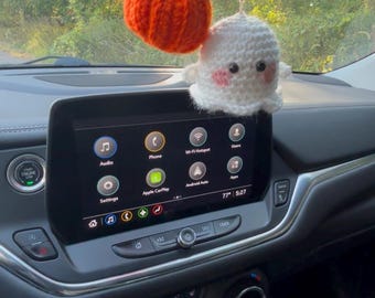 Puede incluir: Amuleto de coche de ganchillo con temática de Halloween. El amuleto incluye una calabaza naranja con un tallo marrón y un fantasma blanco con mejillas rosadas. El amuleto cuelga frente al salpicadero de un coche.