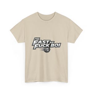 Puede incluir: Camiseta beige con el texto "I'M FAST AS FUCK BOI" en fuente plateada y negra. El diseño incluye un neumático con llamas, sugiriendo un tema de carreras o automovilismo.