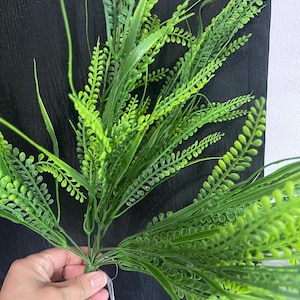 May include: A bunch of artificial green leafy plants with long stems. The stems are tied together with a white string.