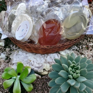 May include: Three handmade soap bars wrapped in clear plastic. The soap bars are in a wicker basket. The soap bars are labeled "Beautiful Pine" and "Hemp".