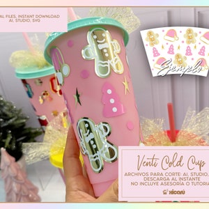 Puede incluir: Un vaso reutilizable para bebidas frías de color rosa y blanco con un diseño de purpurina dorada. El vaso tiene una pajita y una tapa. El diseño incluye hombres de jengibre, árboles de Navidad y estrellas. El texto en el vaso dice "Venti Cold Cup".