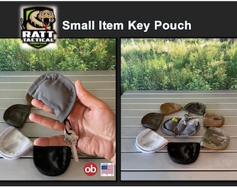 May include: A set of seven small key pouches in various colors and patterns, including gray, black, white, brown, and camouflage. The pouches are made of fabric and have a drawstring closure. The pouches are arranged in a circle on a silver surface. The text "RATT TACTICAL COMBAT GEAR" is visible in the top left corner of the image. The text "Small Item Key Pouch" is visible in the top center of the image.