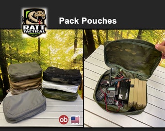 May include: Pack pouches in various camouflage patterns, stacked on a table. The pouches are made by RATT Tactical Combat Gear. One pouch is open, revealing a variety of electronic equipment.