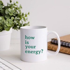 May include: White ceramic mug with a green inscription that reads "how is your energy?"