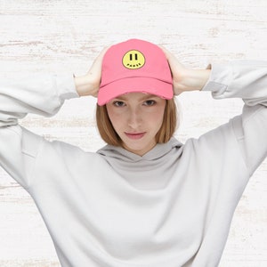 May include: A pink baseball cap with a yellow smiley face and the word "PAUSE" in black text.