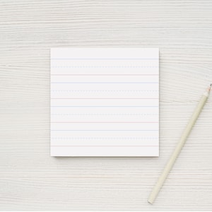 Op de afbeelding: Een wit, gestreept notitieboekje met rode en blauwe lijnen en een potlood op een wit houten oppervlak.