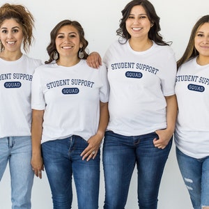 Può includere: Quattro persone indossano magliette bianche con il testo "Student Support Squad" in blu. Sorridono tutte e guardano la fotocamera.