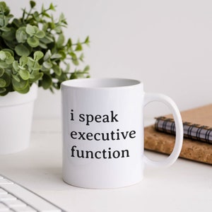 May include: White ceramic coffee mug with black text that reads "i speak executive function".