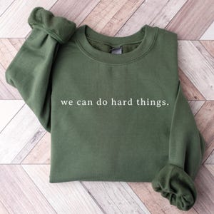 May include: A dark green sweatshirt with the text "we can do hard things." printed in white on the front.