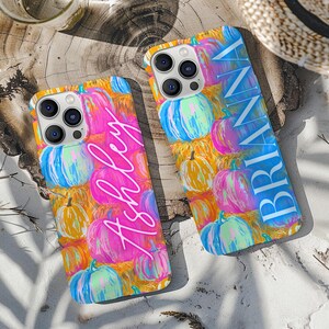 Op de afbeelding: Twee smartphonehoesjes met een kleurrijk pompoenpatroon in roze, blauw, oranje en geel. Het ene hoesje toont de naam Ashley in wit cursief schrift, terwijl het andere de naam BRIANNA in witte blokletters bevat.