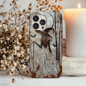 Puede incluir: Funda de teléfono con diseño de bruja. La funda tiene una combinación de colores blanco y marrón con una silueta de bruja, murciélagos y una luna llena. El diseño incluye hojas de otoño y siluetas de árboles, creando un tema de Halloween.