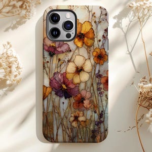 May include: A phone case featuring a floral design with orange, purple, and cream-colored flowers. The case has a glossy finish and a raised camera bump. The flowers are set against a light background with subtle details.