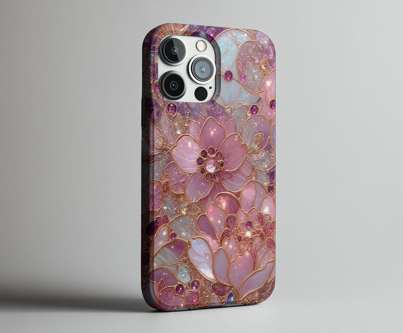 May include: A phone case featuring a floral design in shades of pink, purple, and gold. The case has a glossy finish and is adorned with sparkling accents. The design includes large, stylized flowers and intricate details.