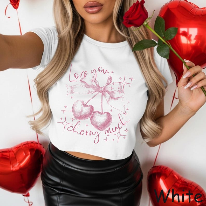 May include: White crop top with a pink cherry graphic and the text "Love you cherry much". The design includes a bow and stars. The model is holding a red rose and heart-shaped balloons.